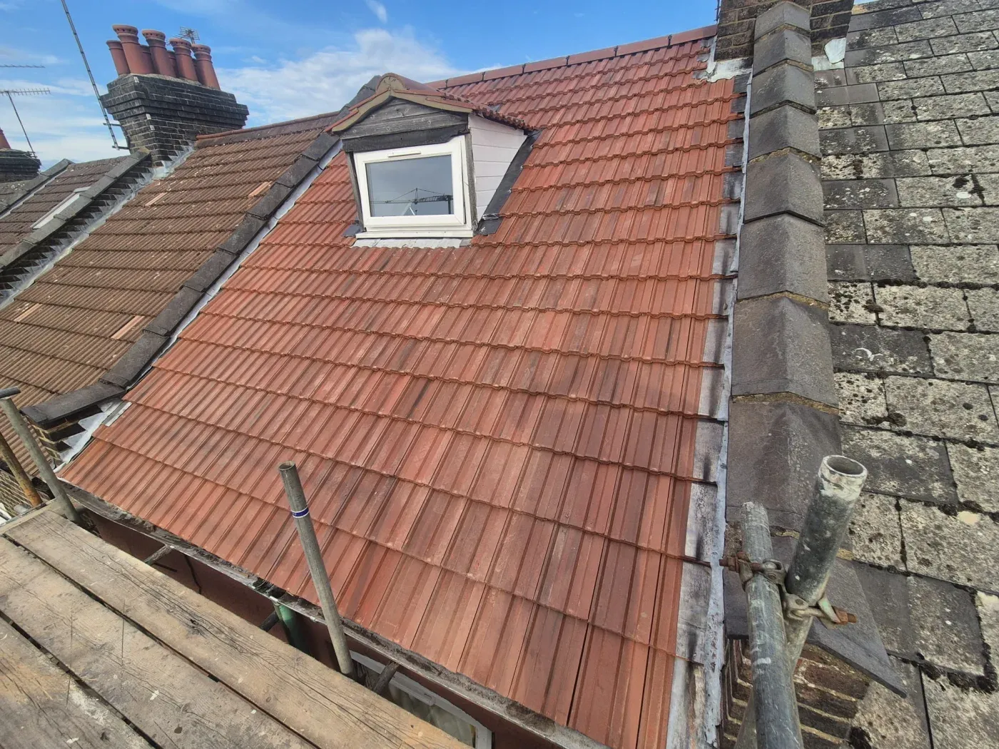 Newly re-tiled roof with red interlocking tiles around a dormer window on a terraced house, completed by Expert Roofing Services