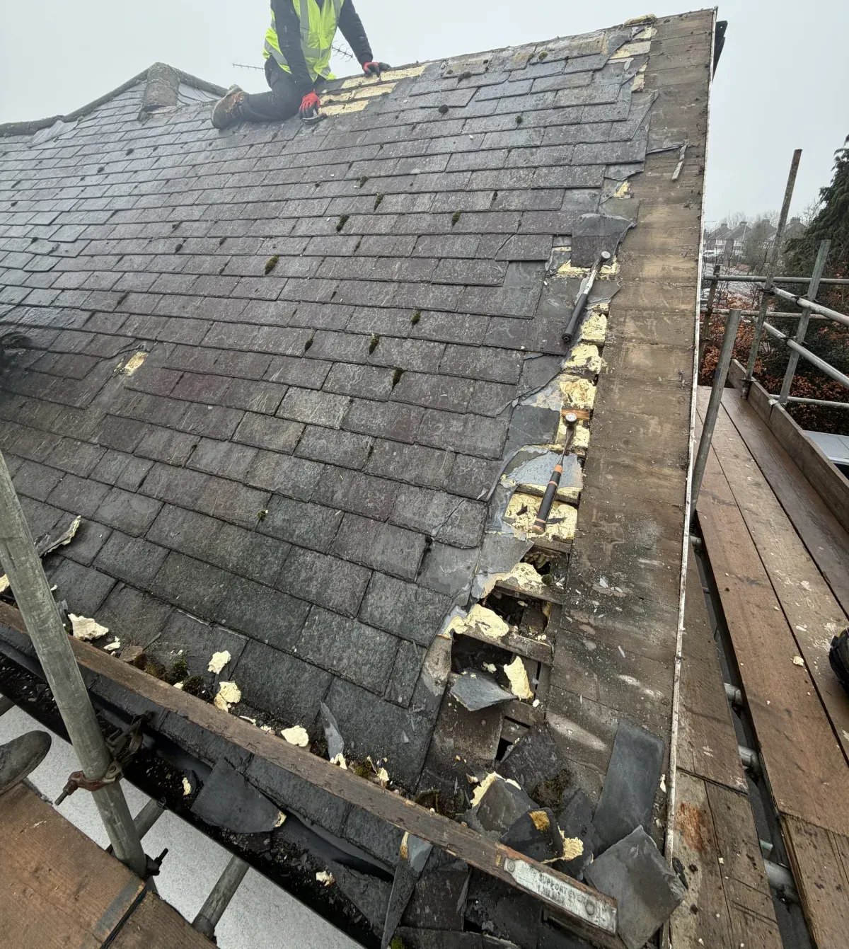 Roofer in hi-vis stripping an old, mossy slate roof on a Windsor & Berkshire home